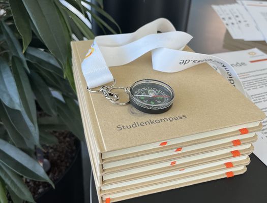Ein Kompass auf einem Stapel Notizbücher mit dem Logo "Studienkompass"
