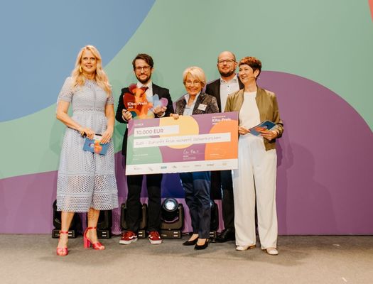 Gruppenbild mit Moderatorin Barbara Schöneberger und Projektbeteiligten. Die Trophäe des 2. Preises sowie ein Scheck über 30.000 Euro Preisgeld werden in die Höhe gehalten.