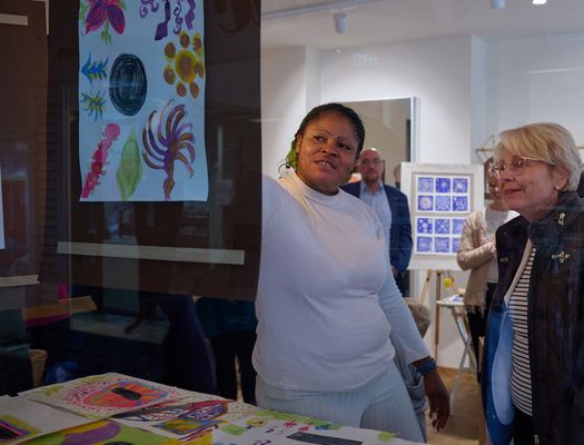 Eine Frau mutmaßlich mit Migrationshintergrund zeigt Bärbel Bergerhoff-Wodopia, Mitglied des Vorstands der RAG-Stiftung, ein aufgehängtes Dokument, auf dem verschiedene bunte Farben und Formen zu sehen sind. 