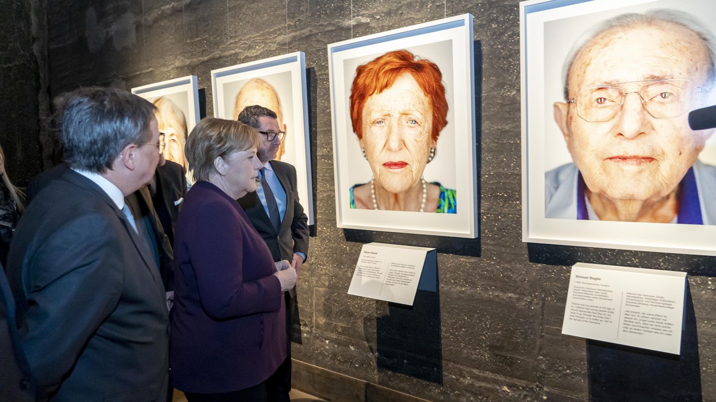 Angela Merkel (zum damaligen Zeitpunkt Bundeskanzlerin) und Armin Laschet (zum damaligen Zeitpunkt NRW-Ministerpräsident) betrachten Portraitaufnahme der Ausstellung zu Holocaust-Überlebenden.