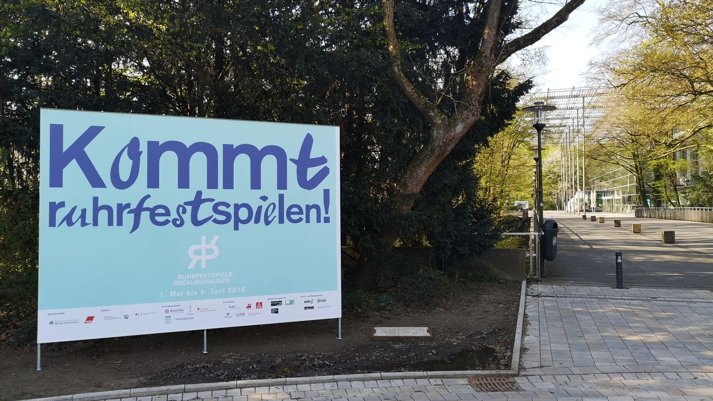 Plakat mit der Aufschrift "Kommt Ruhrfestspielen" vorm Ruhrfestspielhaus