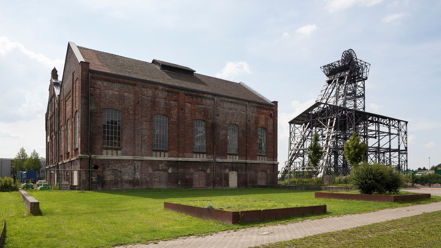 Rötliches Maschinenhaus links, rechts ein Fördergüst; im Vordergrund sattgrüne Wiese