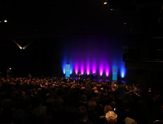 Eine blau-pink angeleuchtete Bühne, davor eine große Menschenmenge im Publikum