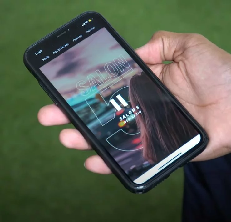 Eine Person hält ein Smartphone in der Hand. Auf diesem ist das Logo von "Salon5" zu sehen.