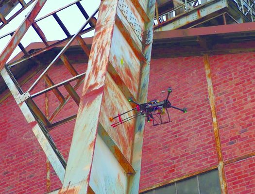 Eine Drohne fliegt dicht neben einem Stahlfördergerüst, an dem sichtbare Rostspuren sind