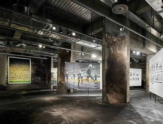 Blick in die Ausstellung zum Thema "Fußball". Es sind großformatige Bilder mit Fußballmotiven zu sehen, unter anderem die "gelbe Wand" des BVB