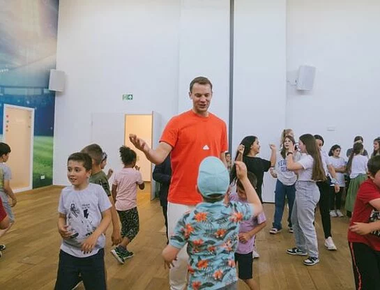 Manuel Neuer interagiert mit Kindern, die in einem größeren Raum spielen.
